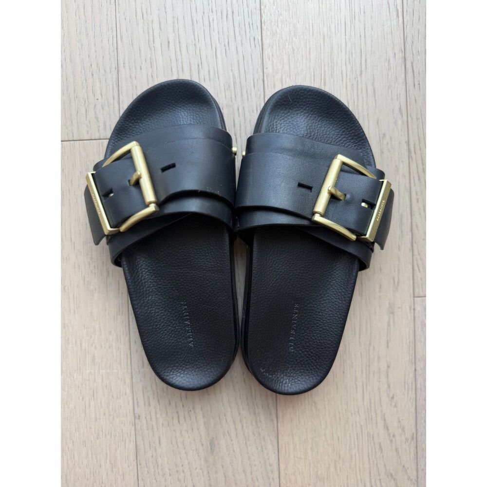 AllSaints black leather sandals with gold-tone buckles.